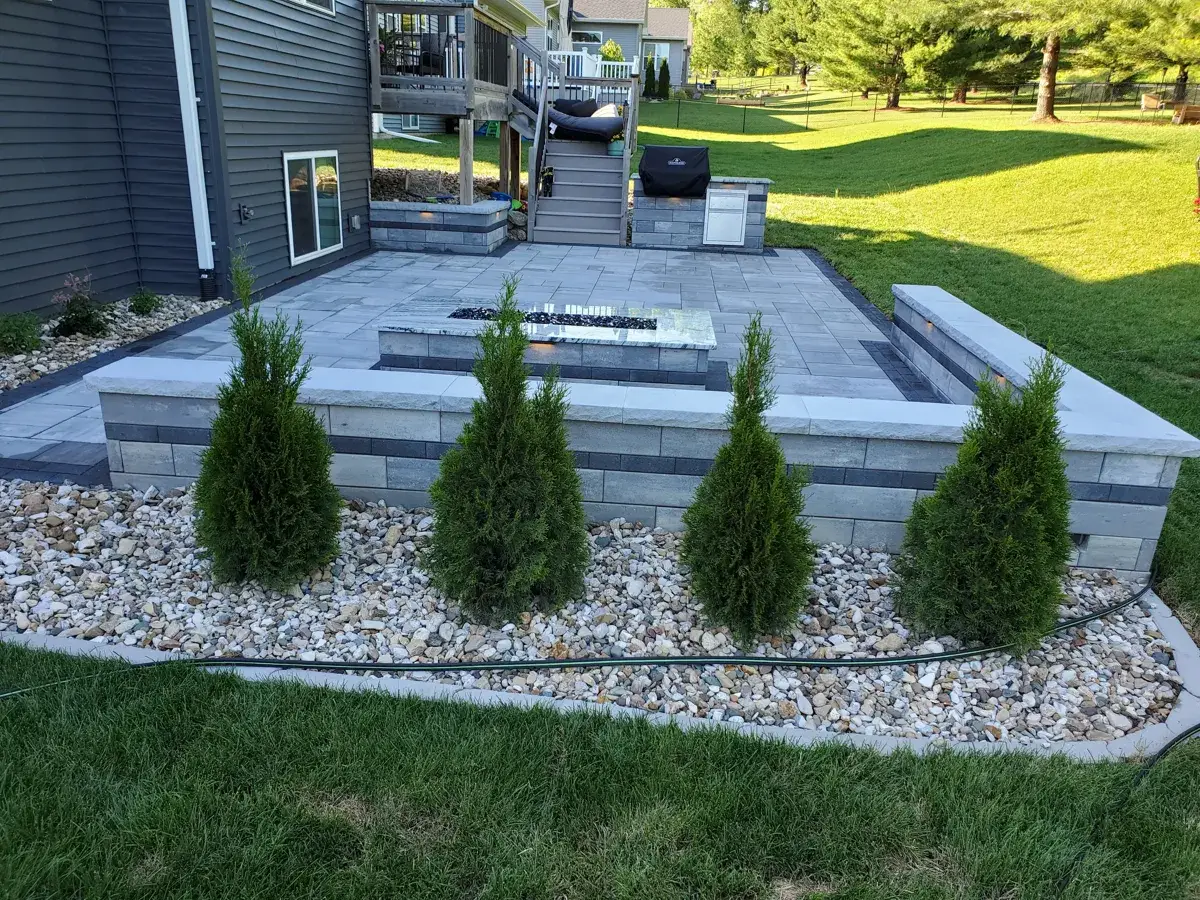 Row of newly planted evergreen shrubs in a white rock bed beside a patio